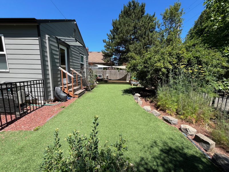 Outdoor classroom with trees, bushes, artificial grass and a line of balancing rocks.